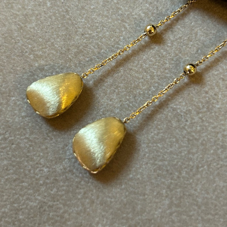 Gold earrings with pebble-like stones on a neutral background