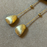 Gold earrings with pebble-like stones on a neutral background