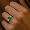Close-up of a hand wearing a ring with a green gemstone on a brown textured background