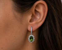 Close-up of an ear wearing a green gemstone earring with a diamond halo.