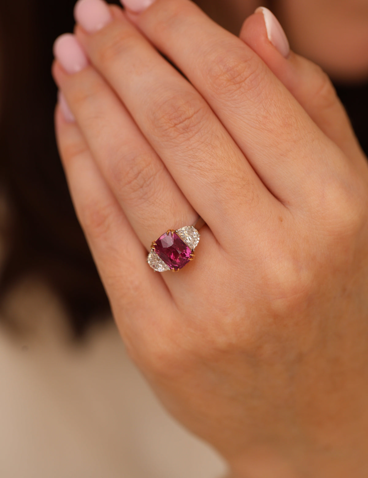 A close-up of a hand wearing a ring with a heart-shaped pink gemstone and small clear accent stones on a gold setting.
