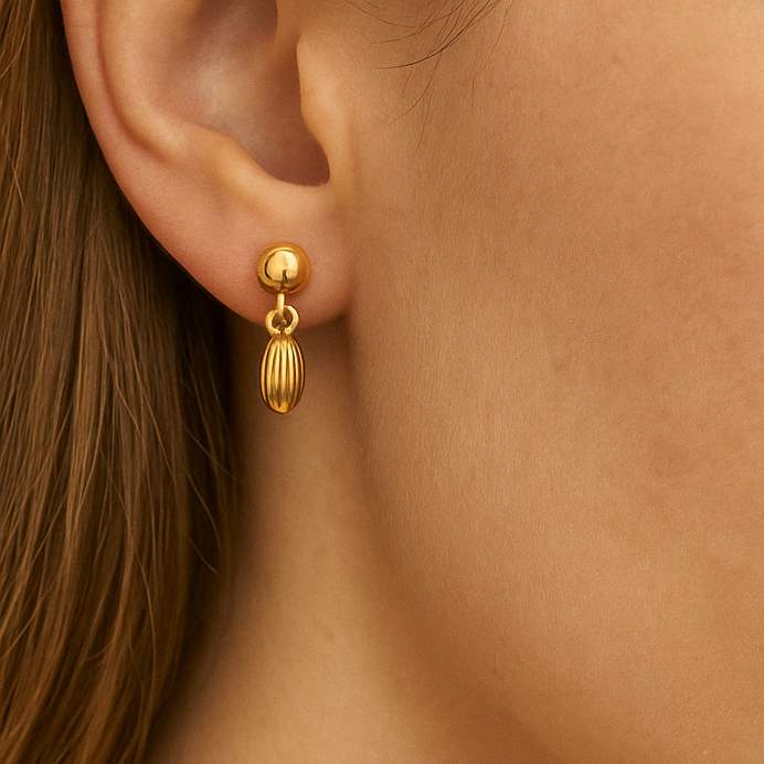Close-up of a person wearing gold earrings with a neutral background